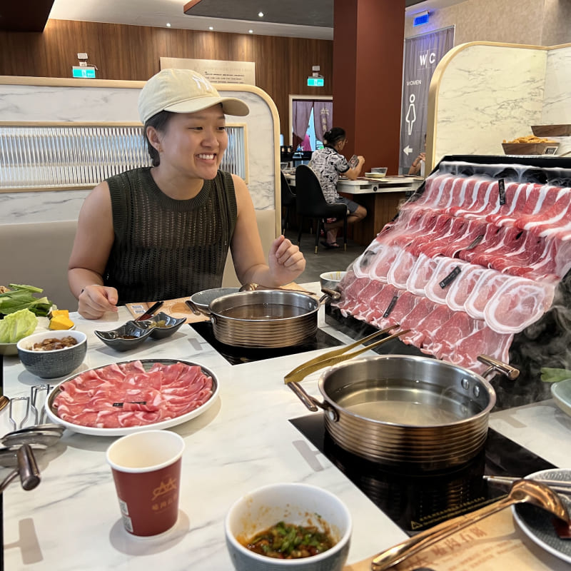 A woman in front of a wall of meat at a hotpot restauratn