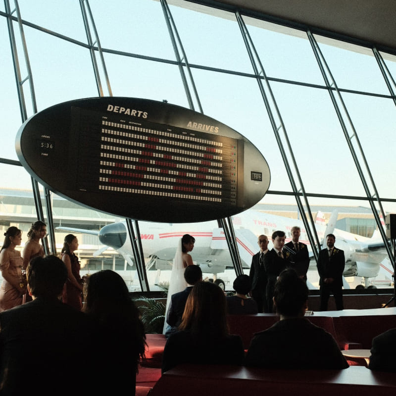 A couple getting married in front of a large sign that says J+J with an airplane in the background