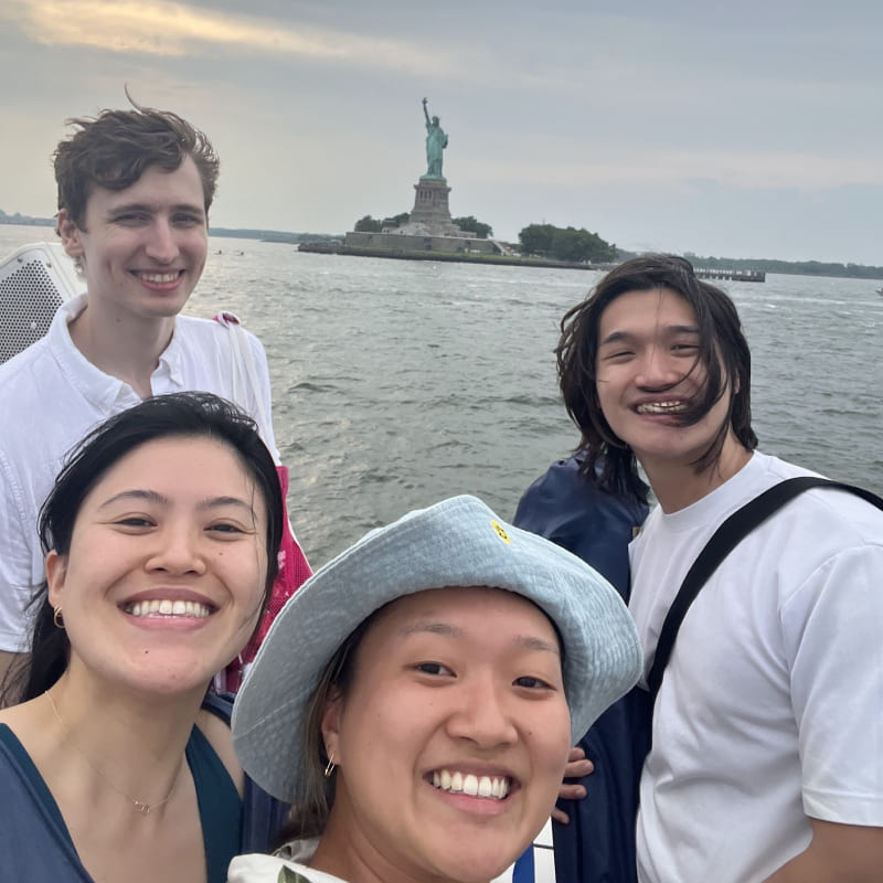 A selfie of 4 people with the Statue of Liberty in the background