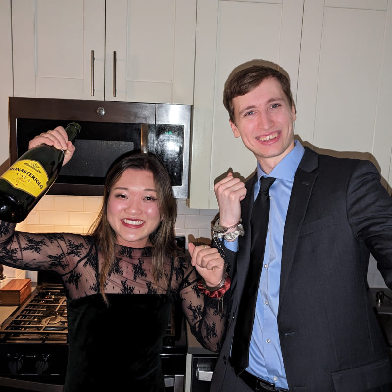 Cindy and Ian dressed nicely holding a bottle of champagne